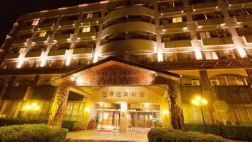 Un hotel de varios pisos con una entrada tradicional, iluminada por luces exteriores.