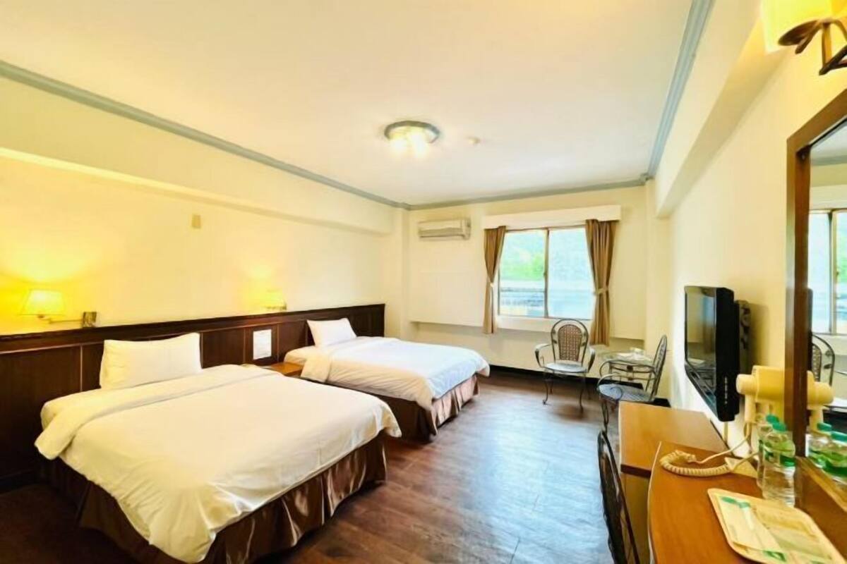 A hotel room with two beds, a desk with a computer, a chair, and a window with curtains.