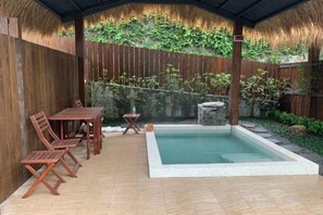 A covered patio with a pool, wooden furniture, and a stone wall with greenery. - Yawan Hotel (Taitung)