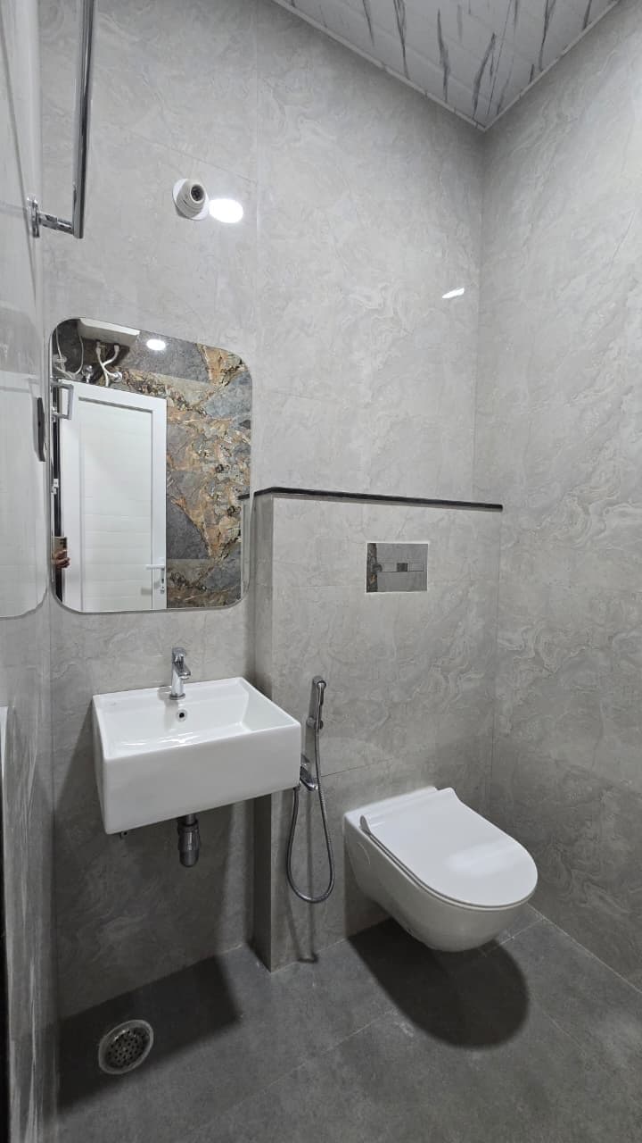 A modern bathroom with a marble wall, a white sink, a handheld showerhead, and a toilet.