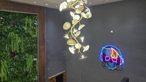 Ein modernes Interieur mit einer außergewöhnlichen Deckenleuchte, einer Neon-Totenköpfige-Dekoration und einer grünen Wand mit hängenden Pflanzen.