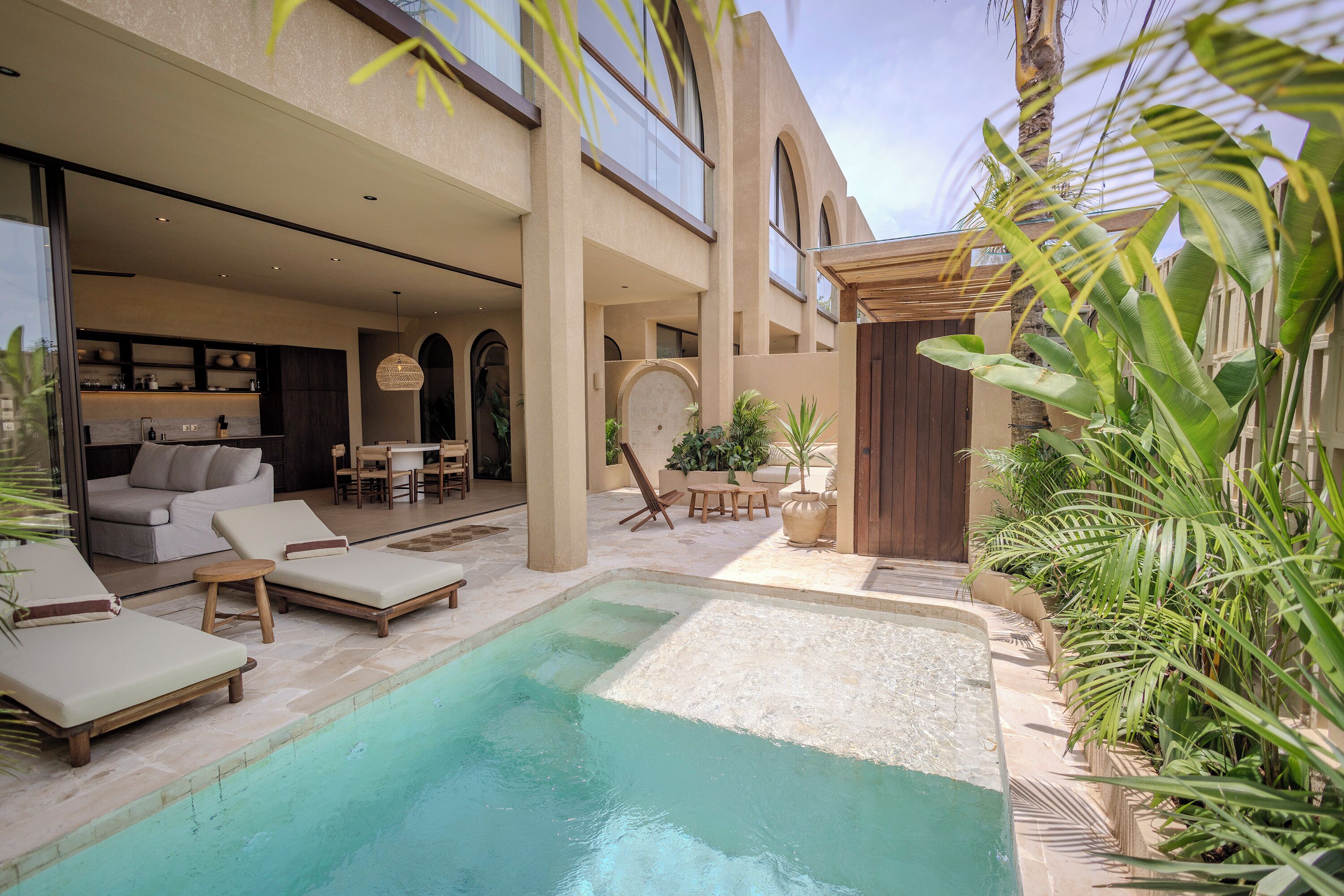 A pool area with lounge chairs, a dining area, and a kitchen visible through an open space.