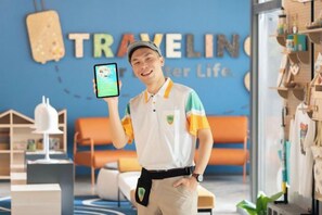 A person holding a smartphone in a room with a blue wall, a wooden shelf with various items, and a sign that reads 'TRAVELING.' - Fullon Poshtel Penghu (Penghu)