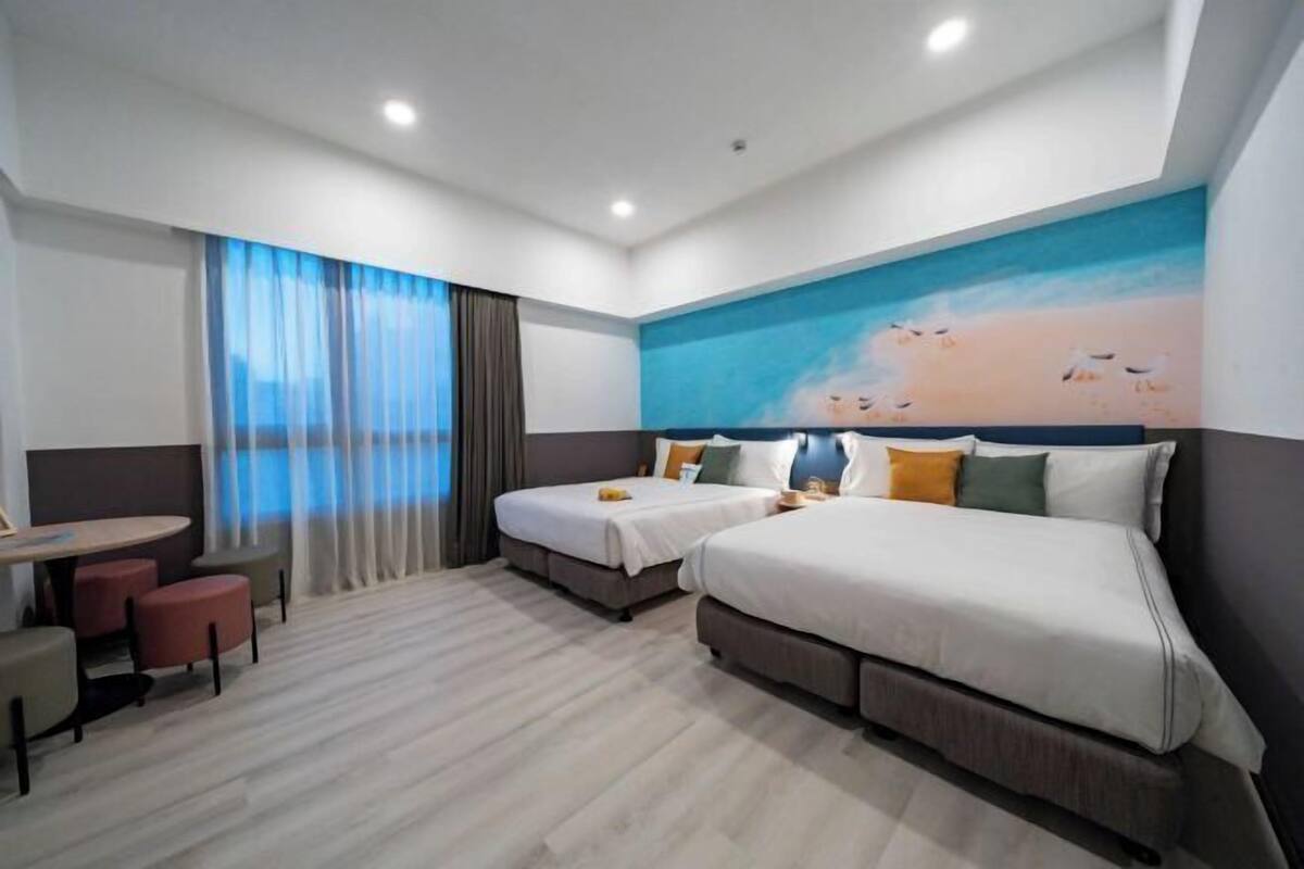A hotel room with two beds, a dining table, and a view of the beach.