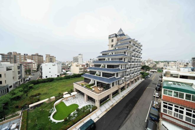 A multi-story residential building with a unique tiered design, surrounded by other buildings and a green space.
