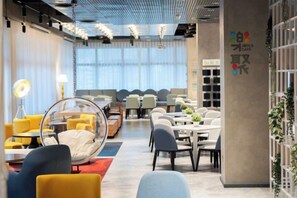 A modern interior with a long dining area, round tables, and chairs, a large window with natural light, and a wall with a logo. - Fullon Poshtel Penghu (Penghu)