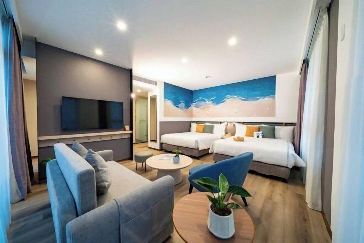 A modern hotel room with a sofa, two beds, a TV, and a painting of a beach scene.