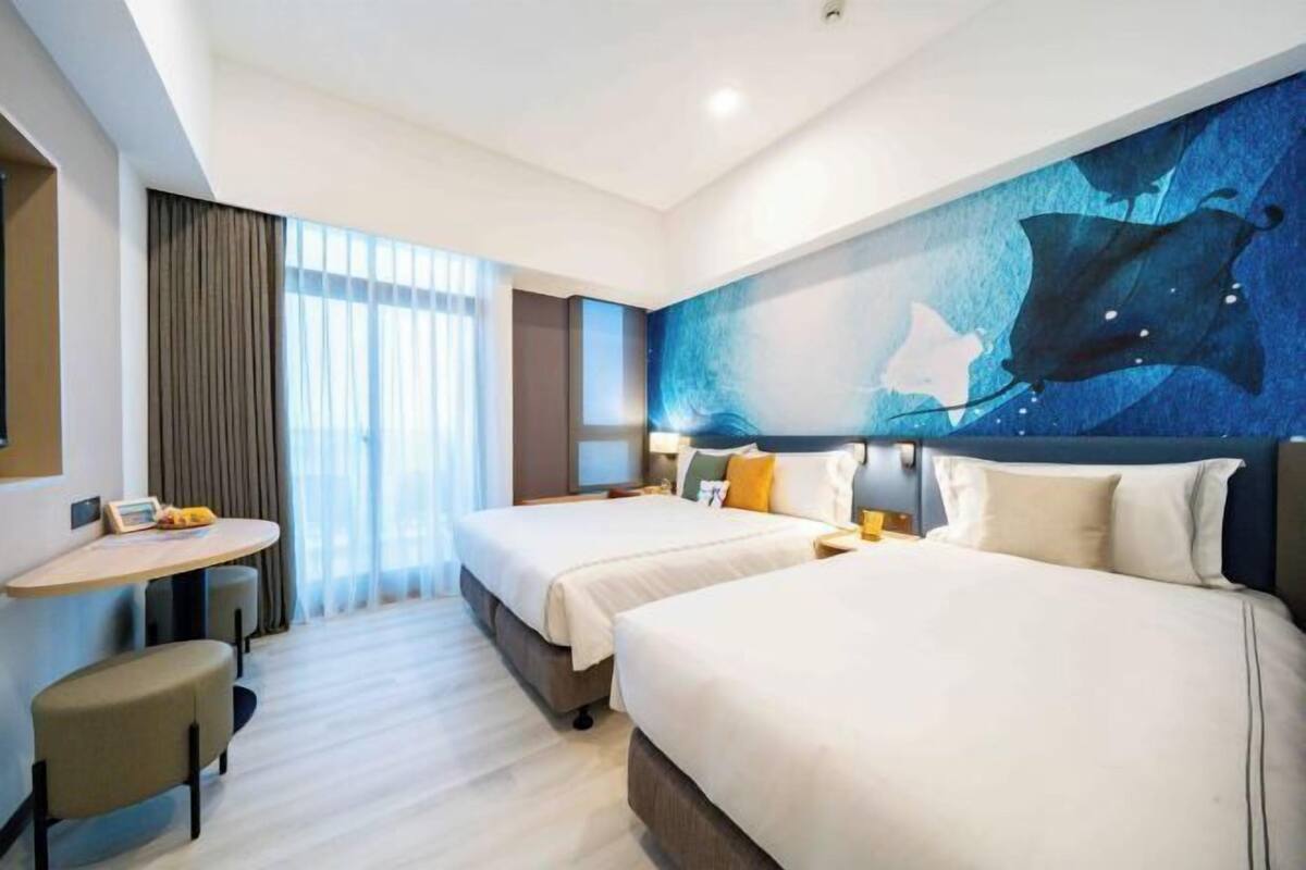 A hotel room with two beds, a desk, and a large wall mural.