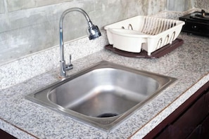 A kitchen sink with a faucet, a dish rack, and a granite countertop. - Me Villa Pererenan (Bali)