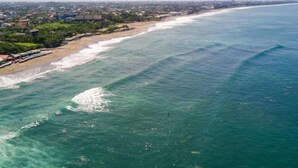 Vista costeira com praia, ondas do oceano e um litoral distante com edifícios.