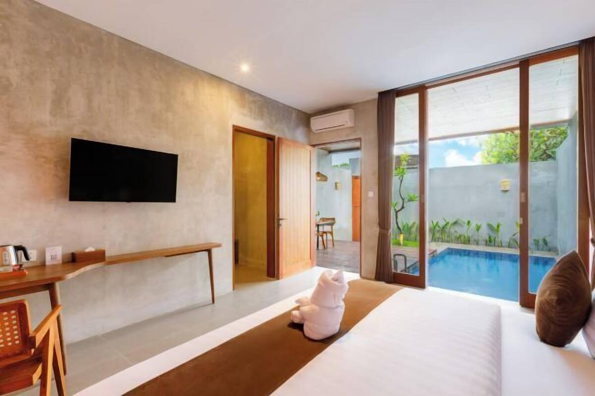 A hotel room with a bed, a desk, a TV, and a view of a swimming pool.