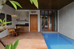A modern kitchen with a dining area, a pool, and a sliding glass door leading to a balcony. - Me Villa Pererenan (Bali)