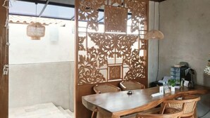 Uma área de refeições com mesa de madeira, cadeiras de vime, um biombô decorativo e um lustre.