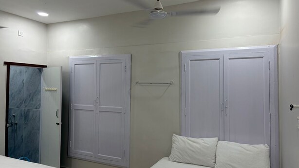 A bedroom with two beds, a ceiling fan, and a door with a towel rack. - Shree Chakra Residency (Kanchipuram)