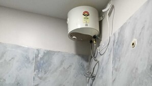 A corner of a bathroom with grey marble tiles and a white water heater mounted on the wall. - Shree Chakra Residency (Kanchipuram)