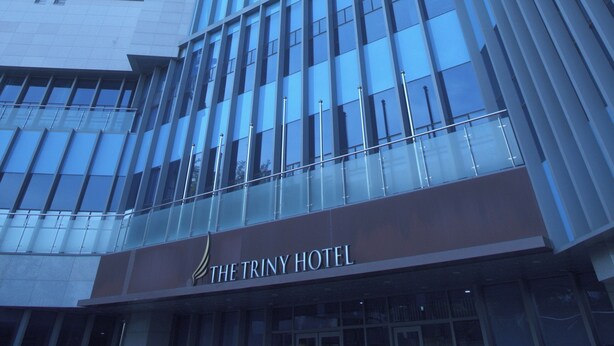 Ein modernes Hotelgebäude mit einer markanten Glasfassade und einem Schild mit der Aufschrift "The Triny Hotel".