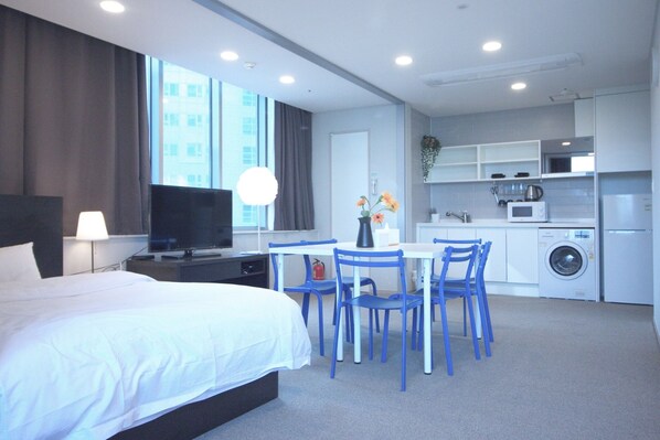 Una habitación de hotel moderna con cama, escritorio, silla, televisor, lavadora y zona de cocina.