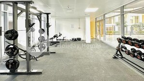A gym with weightlifting equipment, large windows, and a clean, modern design. - Bloomfeilds Central STU  OASIS Masdar (Abu Dhabi)