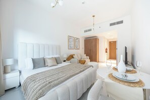 A modern hotel room with a large bed, a sitting area, and a dining table. - Bloomfields Studio in Oasis 1- Masdar (Abu Dhabi)