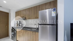 A modern kitchen with wooden cabinets, a stainless steel refrigerator, a washing machine, and a coffee maker. - Bloomfeilds Central STU  OASIS Masdar (Abu Dhabi)