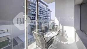 A balcony with wicker chairs and a small table, overlooking a modern building with multiple balconies. - Bloomfeilds Central STU  OASIS Masdar (Abu Dhabi)