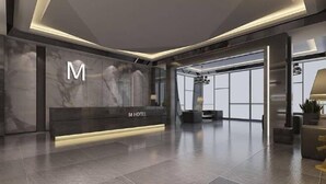 A modern hotel reception area with a marble reception desk, a large 'M' logo, and a spacious lobby with a high ceiling and large windows. - Tsaotun Boutique Hotel (Nantou)