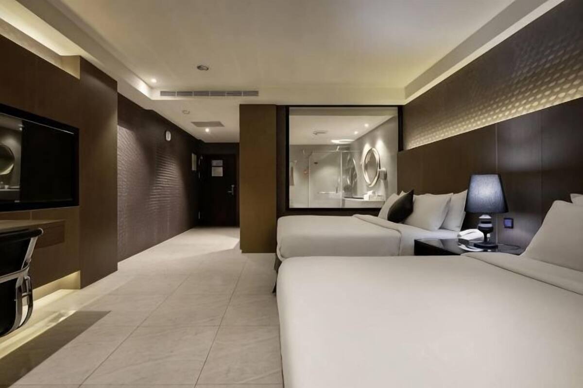 Une chambre d’hôtel avec deux lits, une télévision, un bureau avec une lampe et un grand miroir.