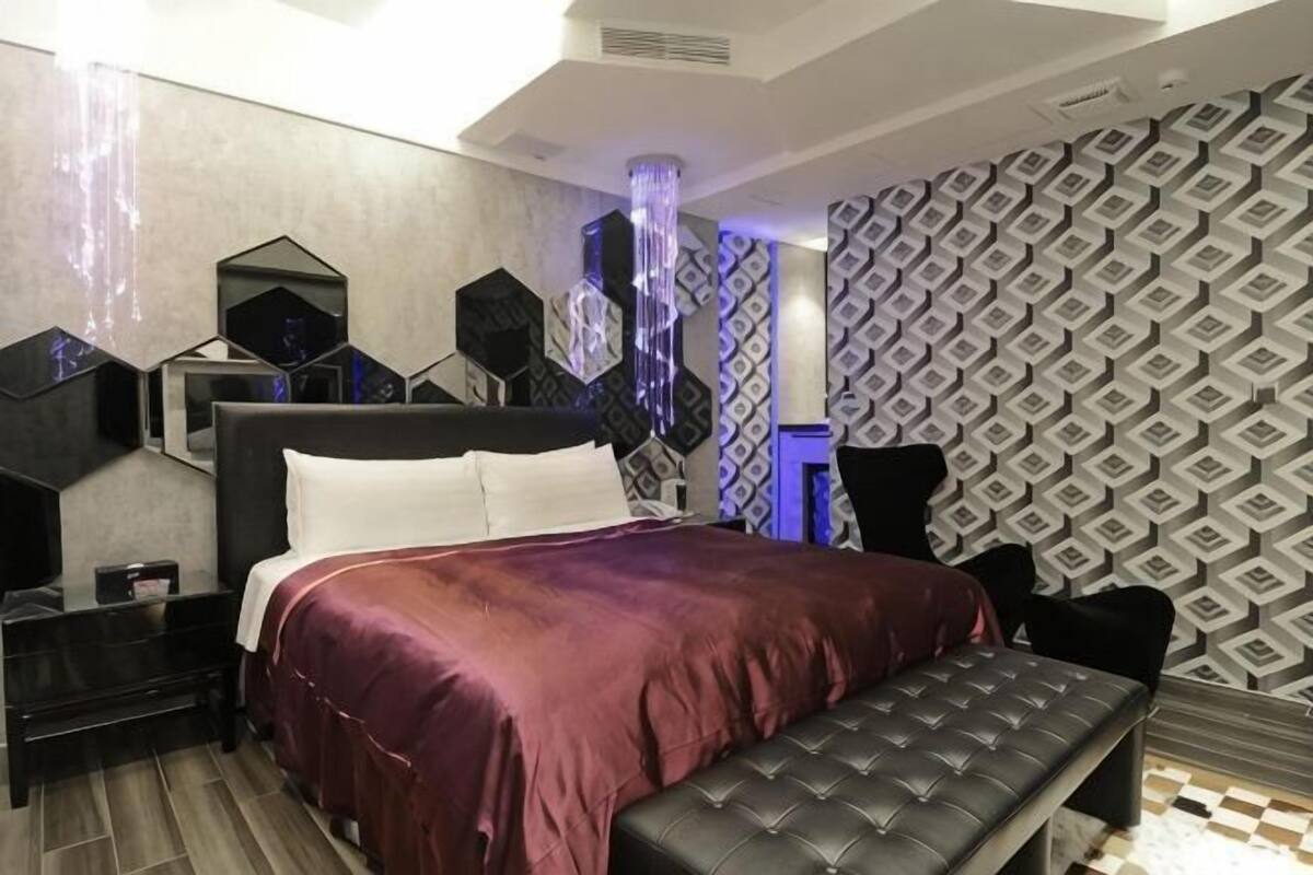 Une chambre à coucher moderne avec un grand lit, un banc, une table de chevet et un mur orné de motifs géométriques.