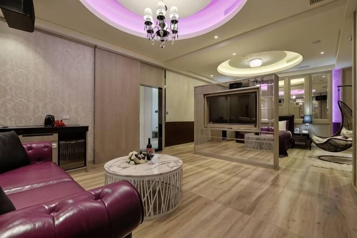 Un salon moderne avec un canapé en cuir, une table basse ronde, un téléviseur à écran plat et un lustre.