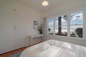 Um quarto com uma cama grande, um guarda-roupa branco, uma mesa consola e uma janela com vista para o mar.