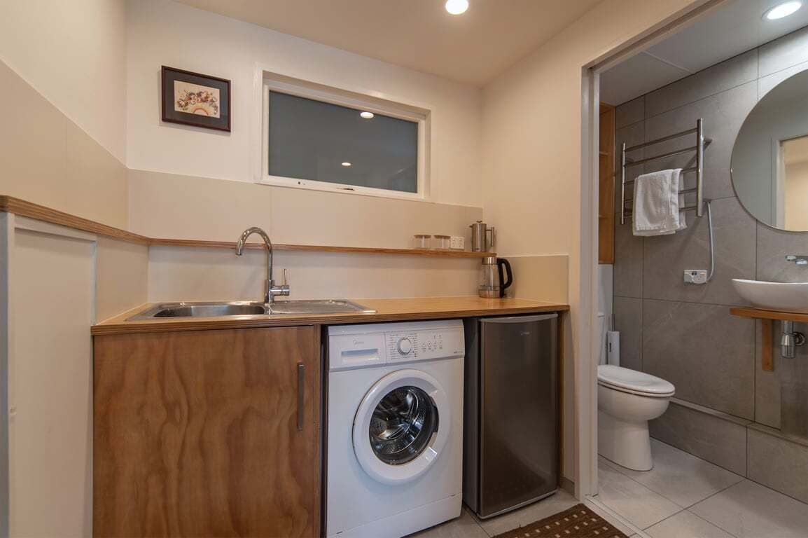 Una cocina compacta con lavadora, lavamanos y una ventana sobre el mostrador.