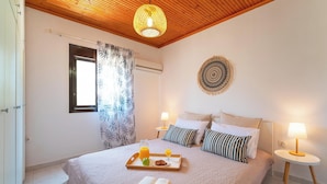 Un dormitorio con cama, lámparas de noche, una bandeja con alimentos para el desayuno, un adorno en la pared y una ventana con cortinas.