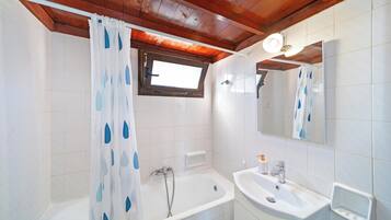 Une salle de bain avec une baignoire, un lavabo, un miroir et une fenêtre.