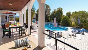 Un espacio al aire libre techado con piscina, sillas de descanso y una mesa de comedor con sillas.