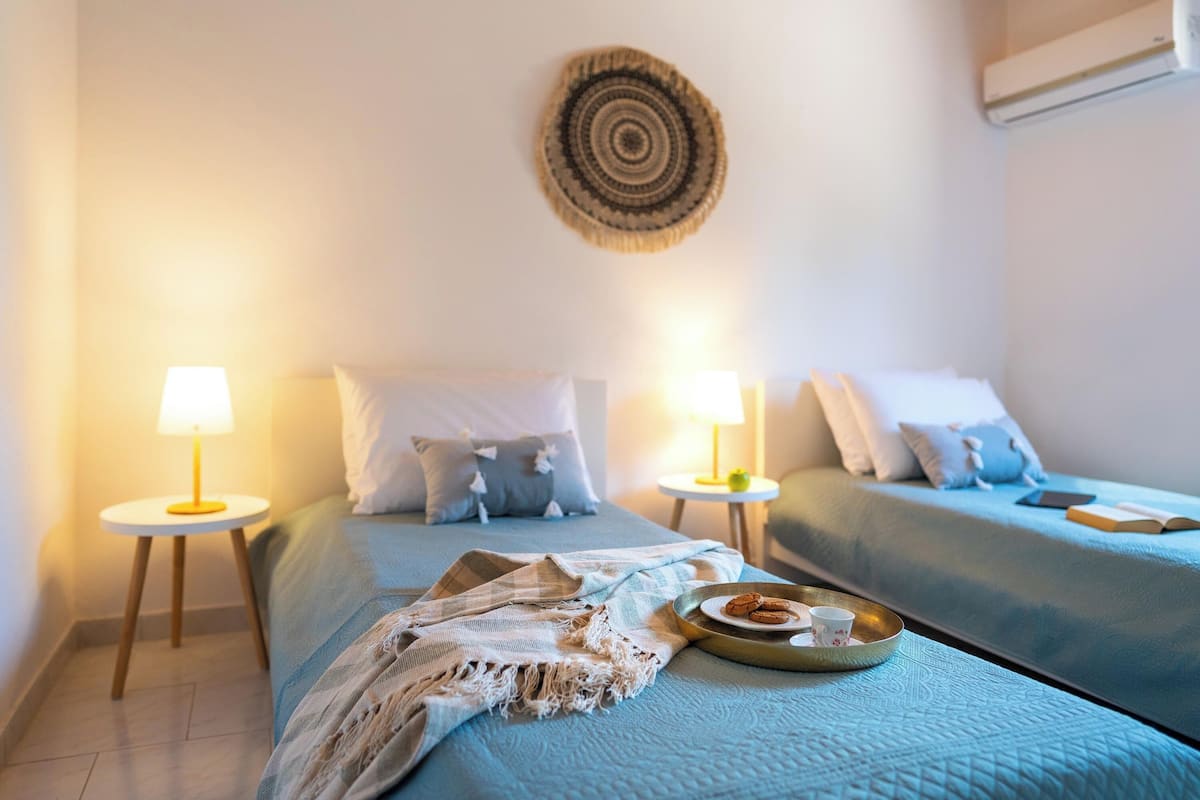 A bedroom with two beds, each with a lamp, a wall hanging, and a tray with cookies and a cup on the bed.