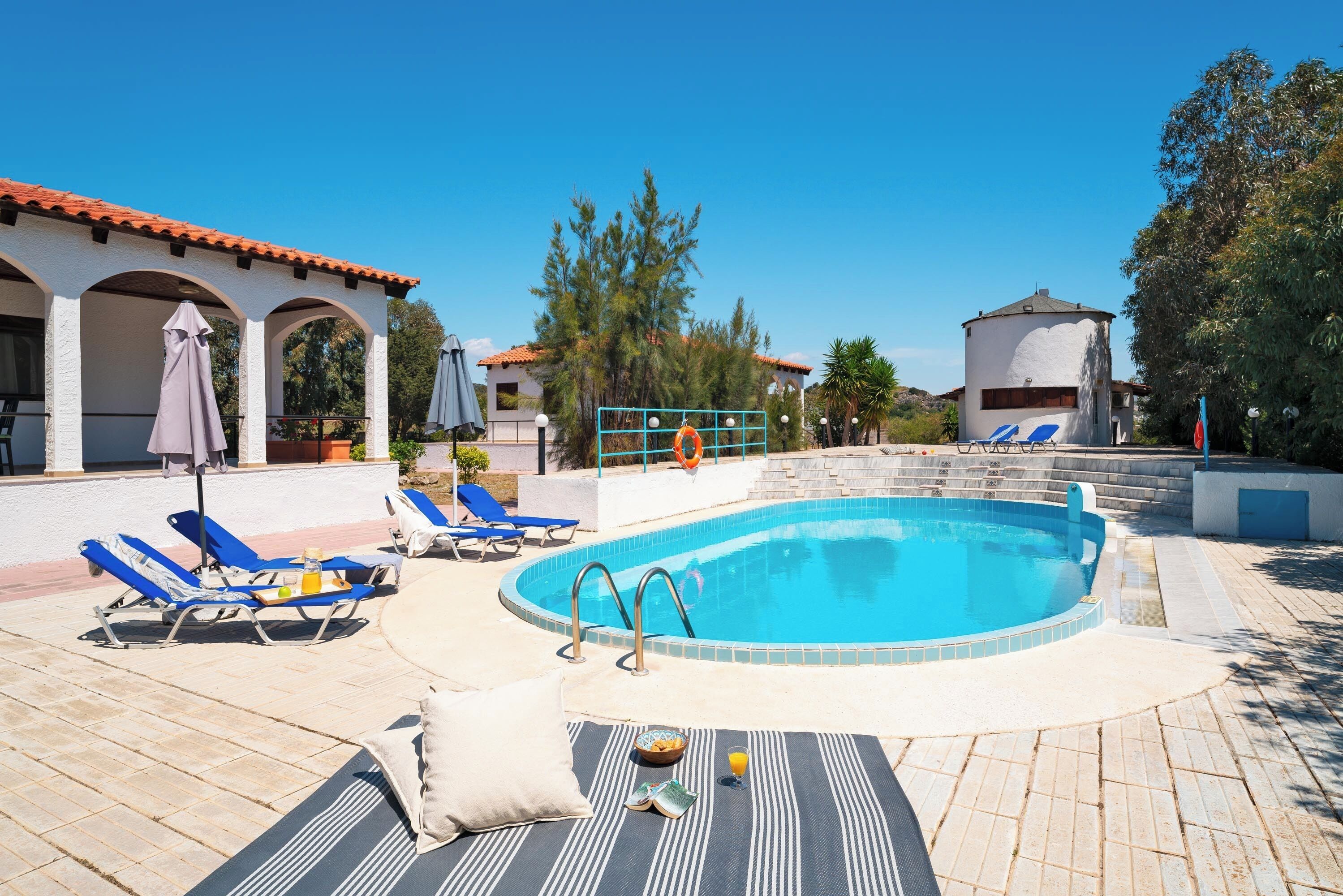 A swimming pool with lounge chairs and umbrellas, surrounded by buildings and trees.