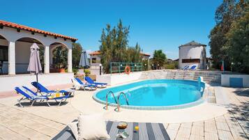 A swimming pool with lounge chairs and umbrellas, surrounded by buildings and trees.