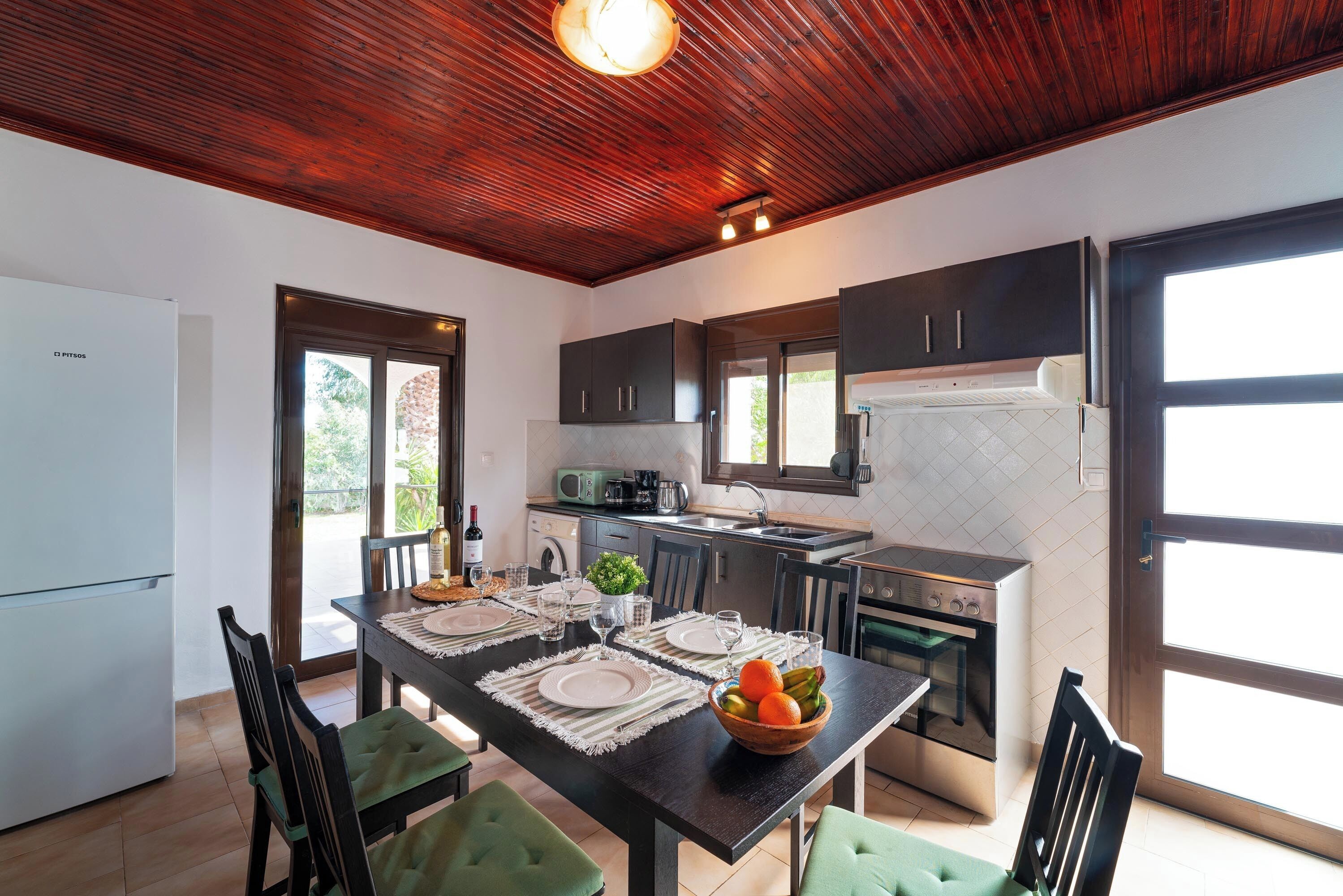 A modern kitchen with dark cabinets, a central island, and a dining area with green chairs.