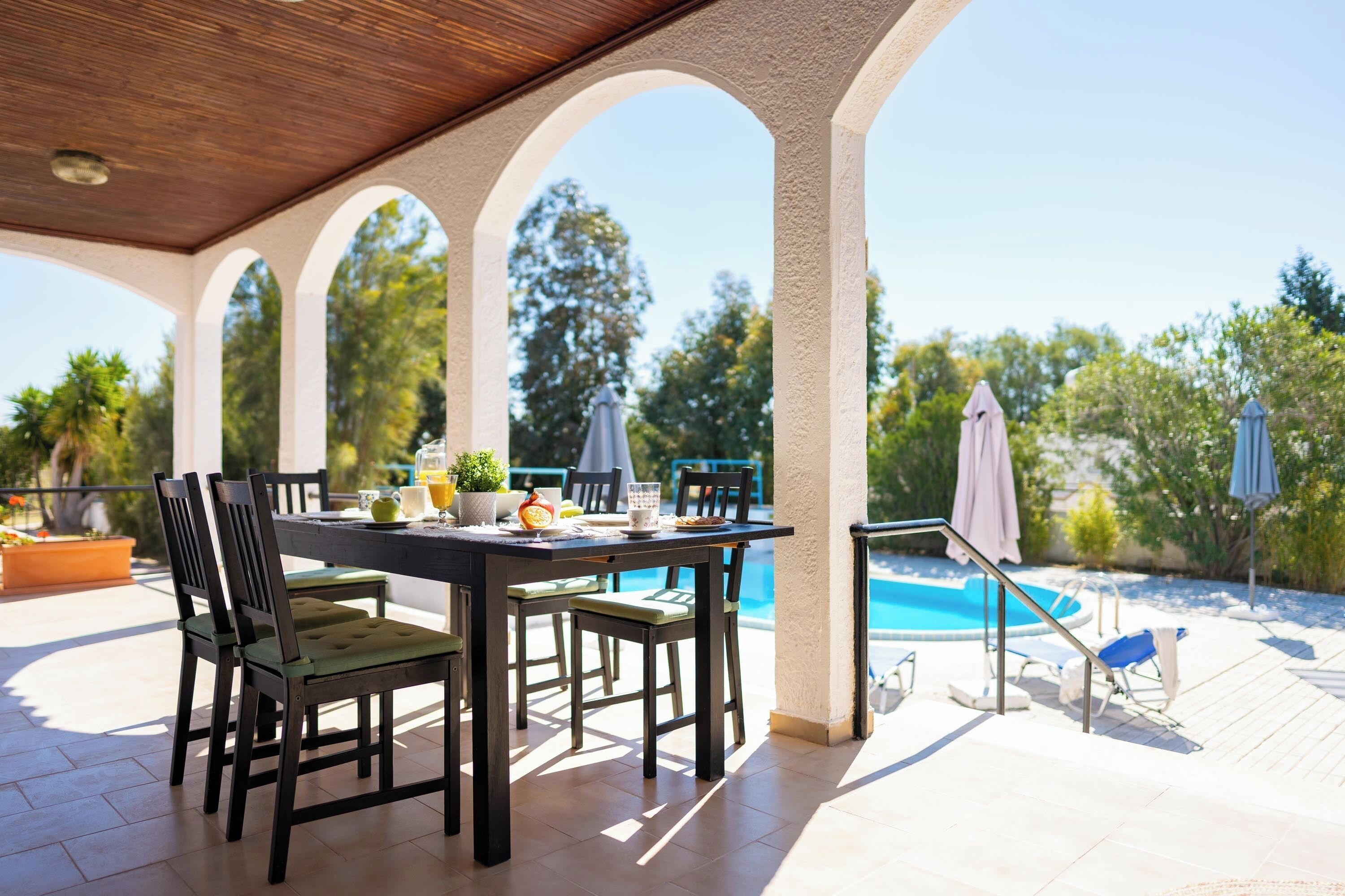 Un patio al aire libre con piscina, una mesa de comedor con sillas y sombrillas.