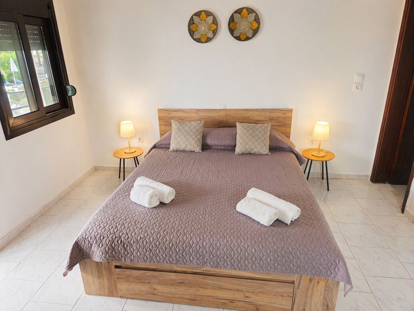 A bed with a wooden headboard, two bedside lamps, and two decorative wall pieces.