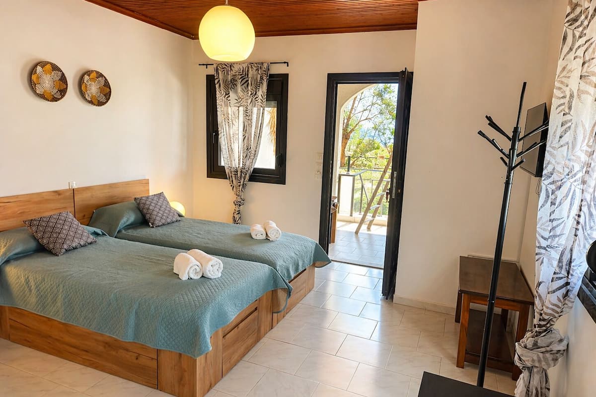 A bedroom with two beds, a wooden ceiling, a chandelier, a balcony with a view, and a coat rack.