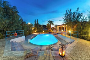 Una piscina con un bordeado, sillas de descanso y un farol.