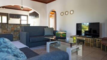 A modern living room with a sofa, a glass coffee table, a TV, and a stone fireplace.