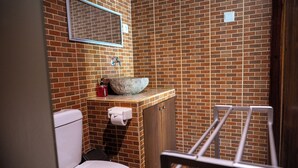 Ein Badezimmer mit Backsteinwand, einem großen Waschbecken, einer Toilette und einem Metallregal.