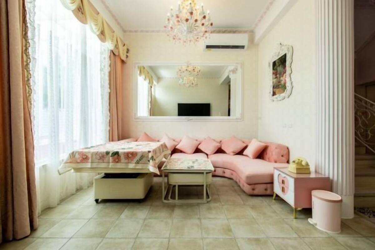 A cozy bedroom with a pink sofa, a small table, and a bedside table with a lamp.