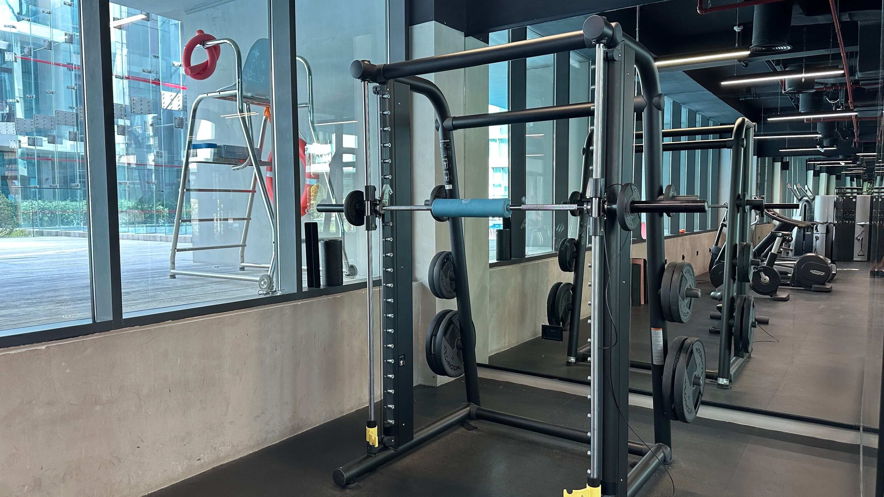 A gym with weightlifting equipment, large windows, and a concrete floor.