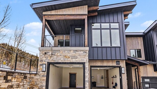 Una casa moderna de dos pisos con fachada de piedra, un balcón y un garaje.
