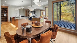 A modern kitchen with a dining area, large windows, and a view of trees. - Ski In on Whitefish Mountain 3 BD 3BA Sleeps 12 Incredible SKI Access (Whitefish)