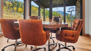 Un salón de conferencias con una gran mesa y cuatro sillas, ventanas amplias con vistas a un paisaje montañoso y una pared de piedra.