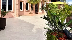 Una casa grande de dos pisos con techo curvo, muchas ventanas y camino de entrada pavimentado.